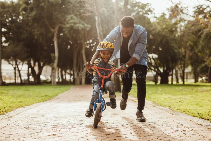 Boy learning to ride a bicycle with his father in park. Father teaching his son cycling at park. Boy learning to ride a bicycle with his father in park. Father teaching his son cycling at park